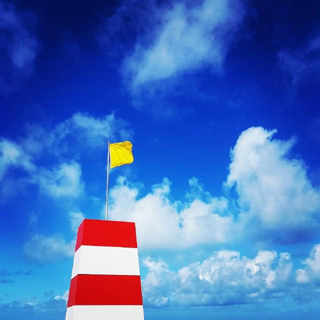 Vind Et hvit og rødt stripete tårn med et gult flagg på toppen mot dyp blå himmel.