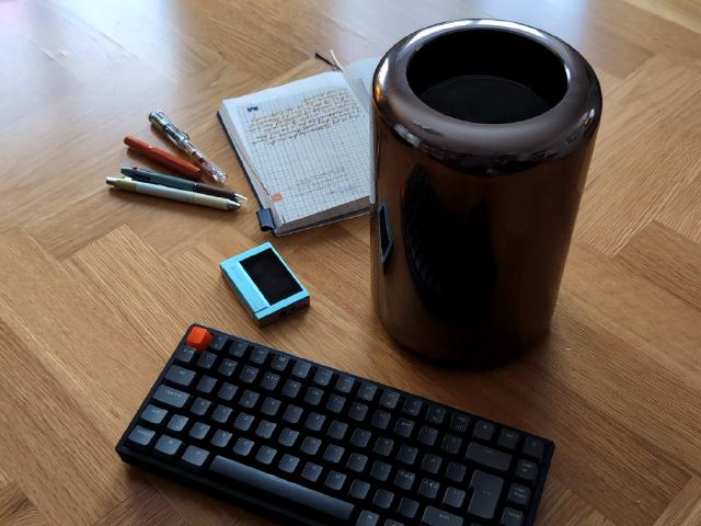 Mac Pro on a table surrounded by keyboard, notes and pens.
