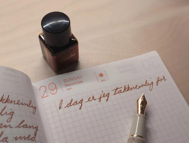 Journalen oppslått med fyllepenn og blekkrus ved siden av, og setningen 'i dag er jeg takknemlig for' skrevet i toppen.