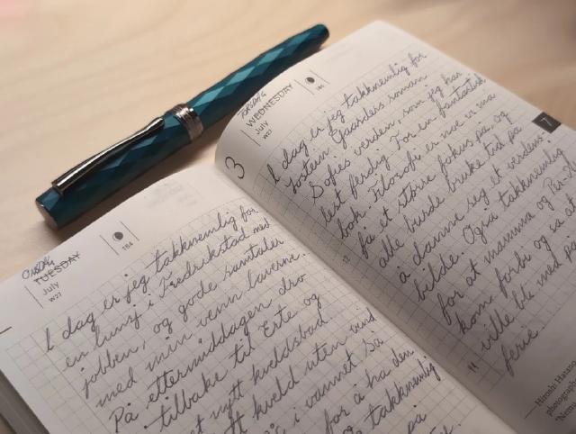 Oppslått notatbok med en fyllepenn liggende over.